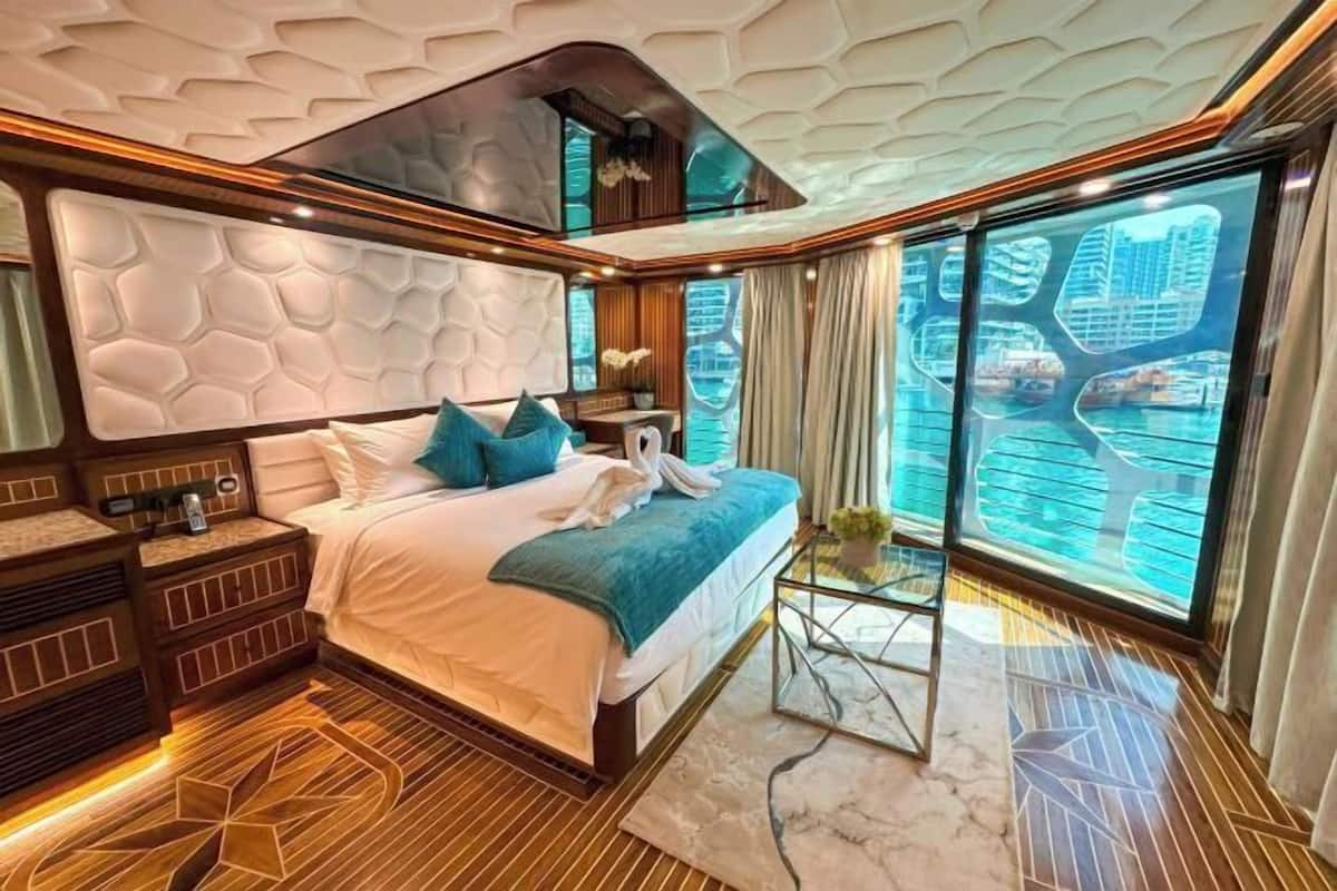 A luxurious bedroom with a large bed, a nightstand, a glass coffee table, and a view of a cityscape through large windows.