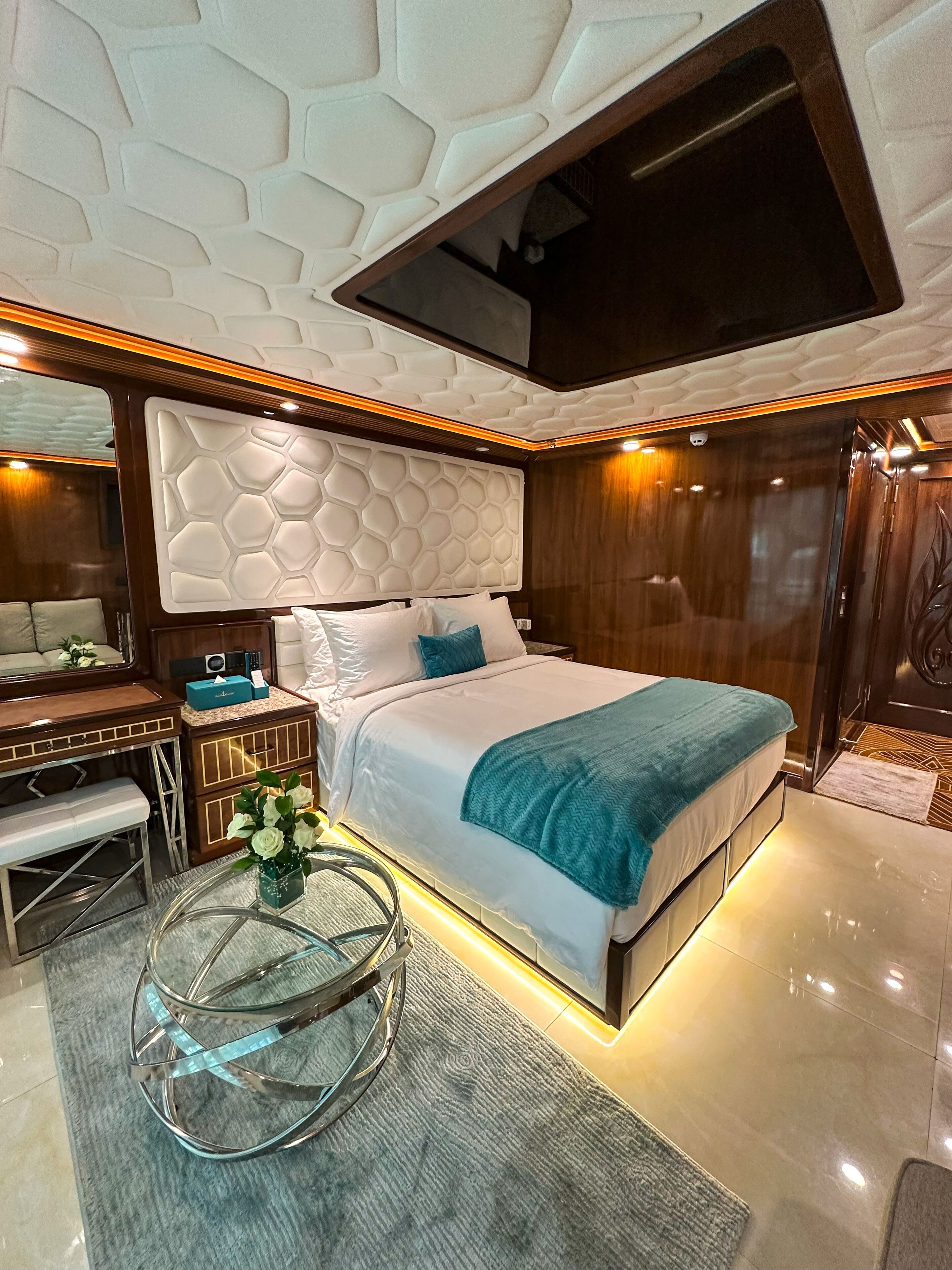 A modern bedroom with a large bed, a desk, and a TV mounted on the ceiling.