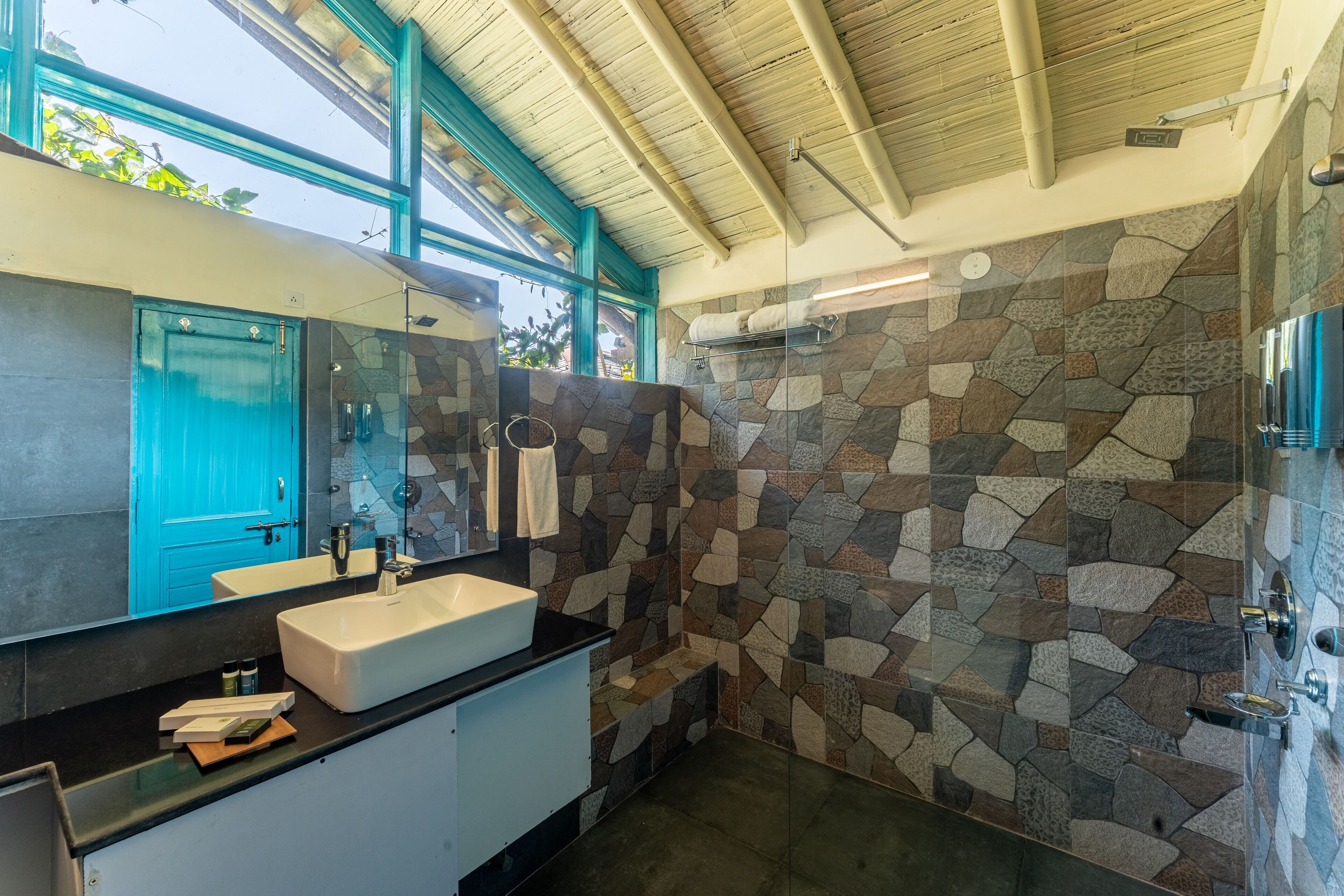 Un baño moderno con ducha de pared de piedra, un espejo grande y una puerta azul.