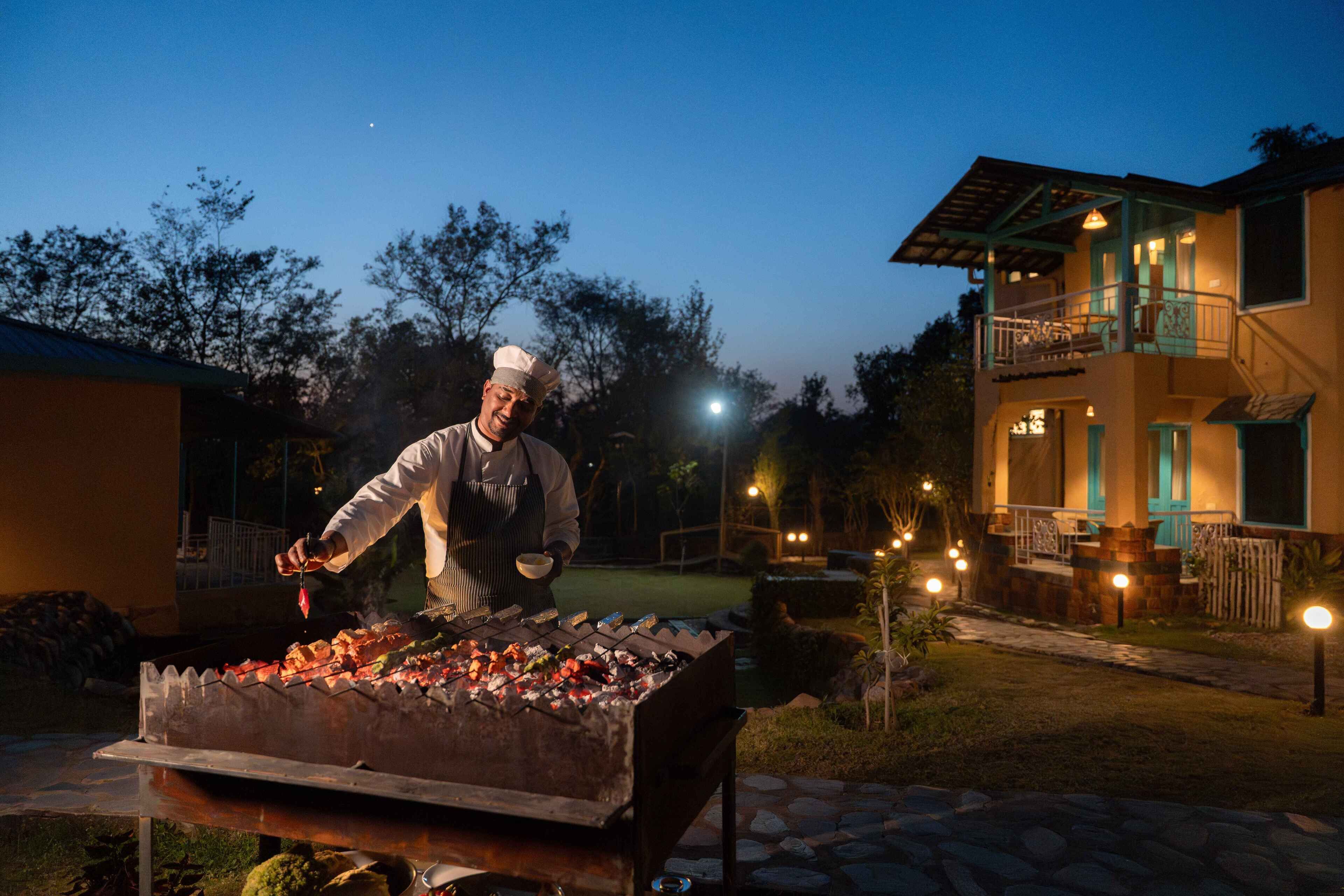 A chef grilling outdoors at night with a house in the background.