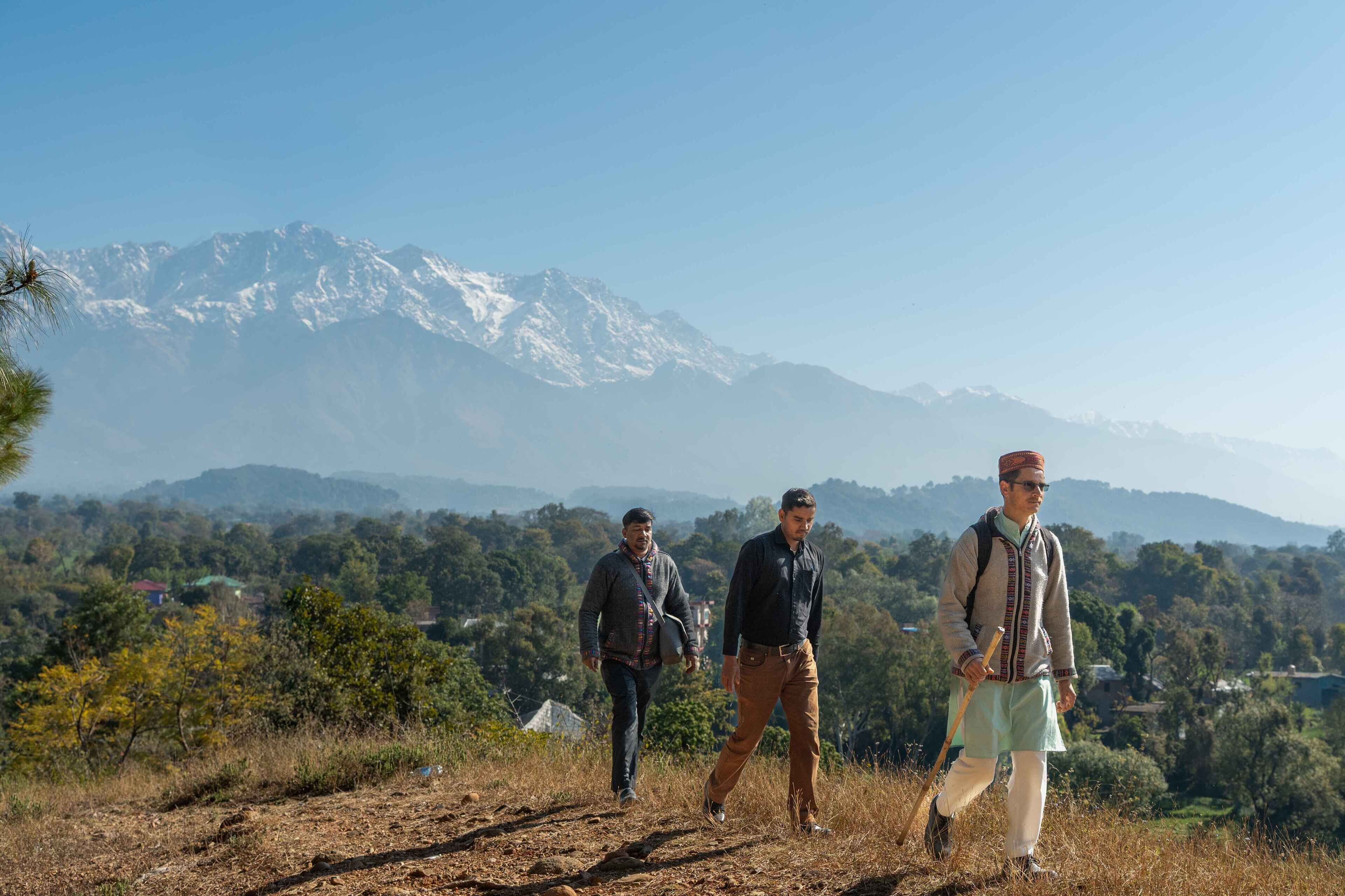 Tres personas caminando por una ladera con una cadena montañosa al fondo.