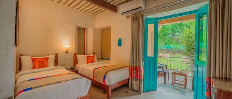 A hotel room with two beds, a balcony with a table and chairs, and a view of greenery outside.
