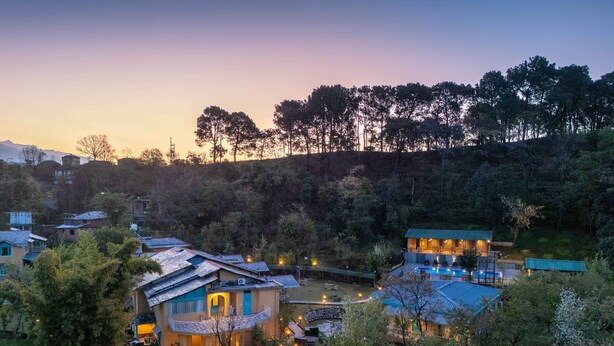 A hillside property with multiple buildings, including a main house with a balcony and a pool area. - Tree of Life Birdsong Chalets (Dharamshala)