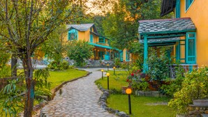 A stone pathway leading to a yellow building with a green porch and blue accents. - Tree of Life Birdsong Chalets (Dharamshala)