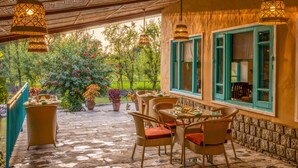 An outdoor patio with wicker furniture and hanging lamps, overlooking a garden with red flowers and greenery. - Tree of Life Birdsong Chalets (Dharamshala)