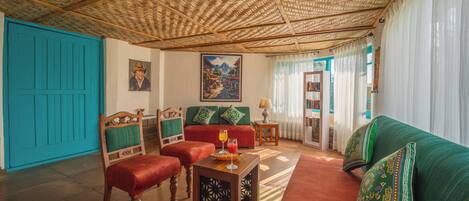 A living room with a woven ceiling, a turquoise door, a red sofa, and a wooden coffee table with a glass and a book.