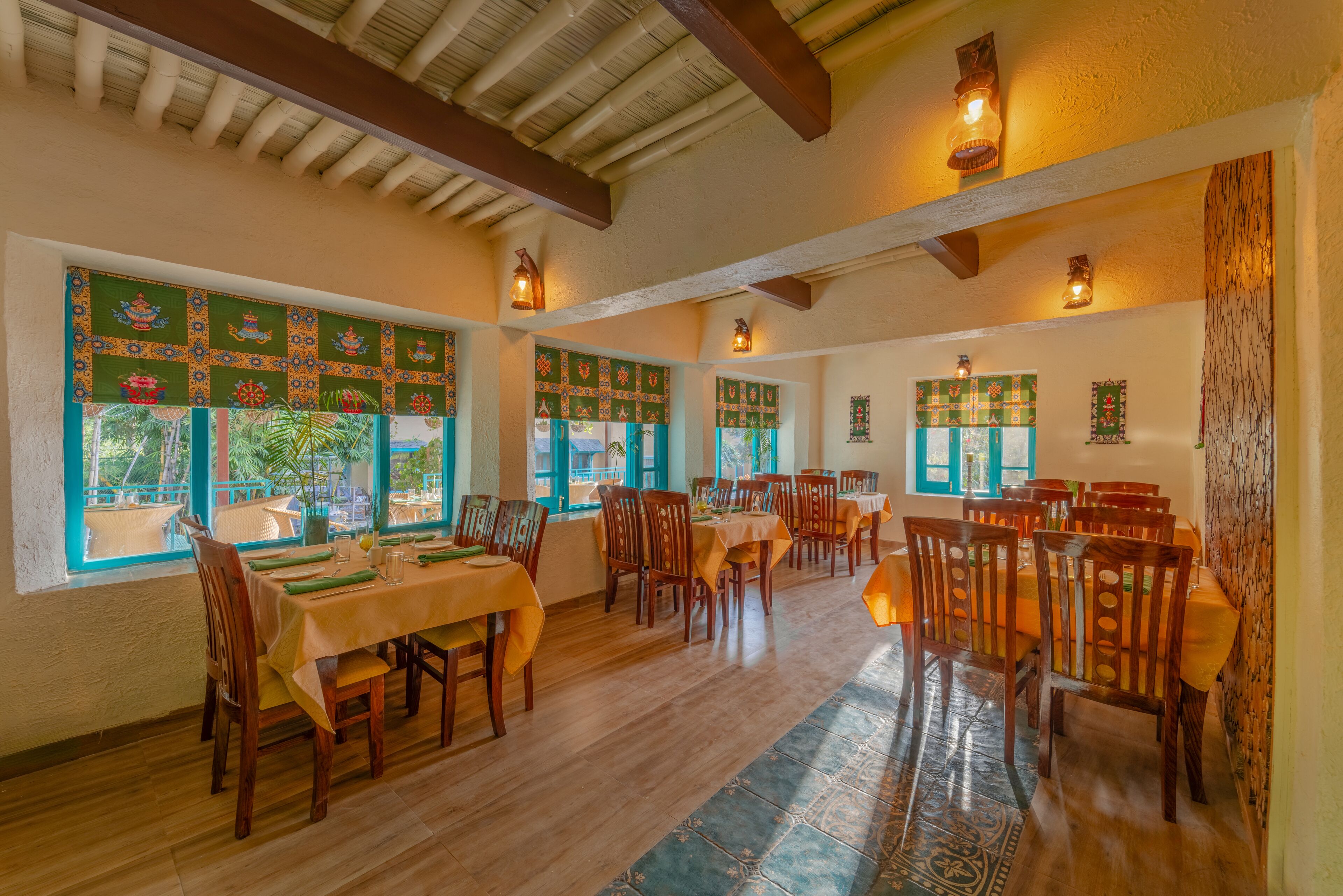 A dining area with multiple tables and chairs, large windows with decorative panels, and wooden beams on the ceiling.