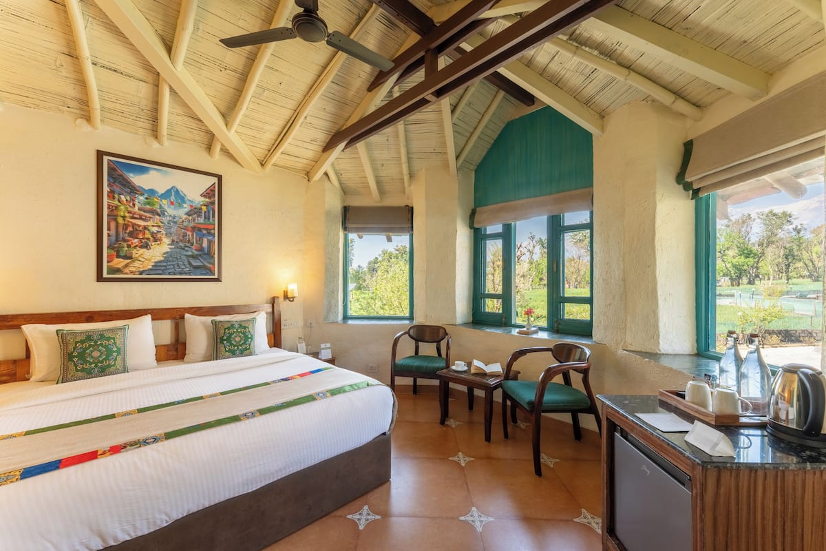 A hotel room with a large bed, a desk, two chairs, a painting on the wall, and a view of the outdoors.