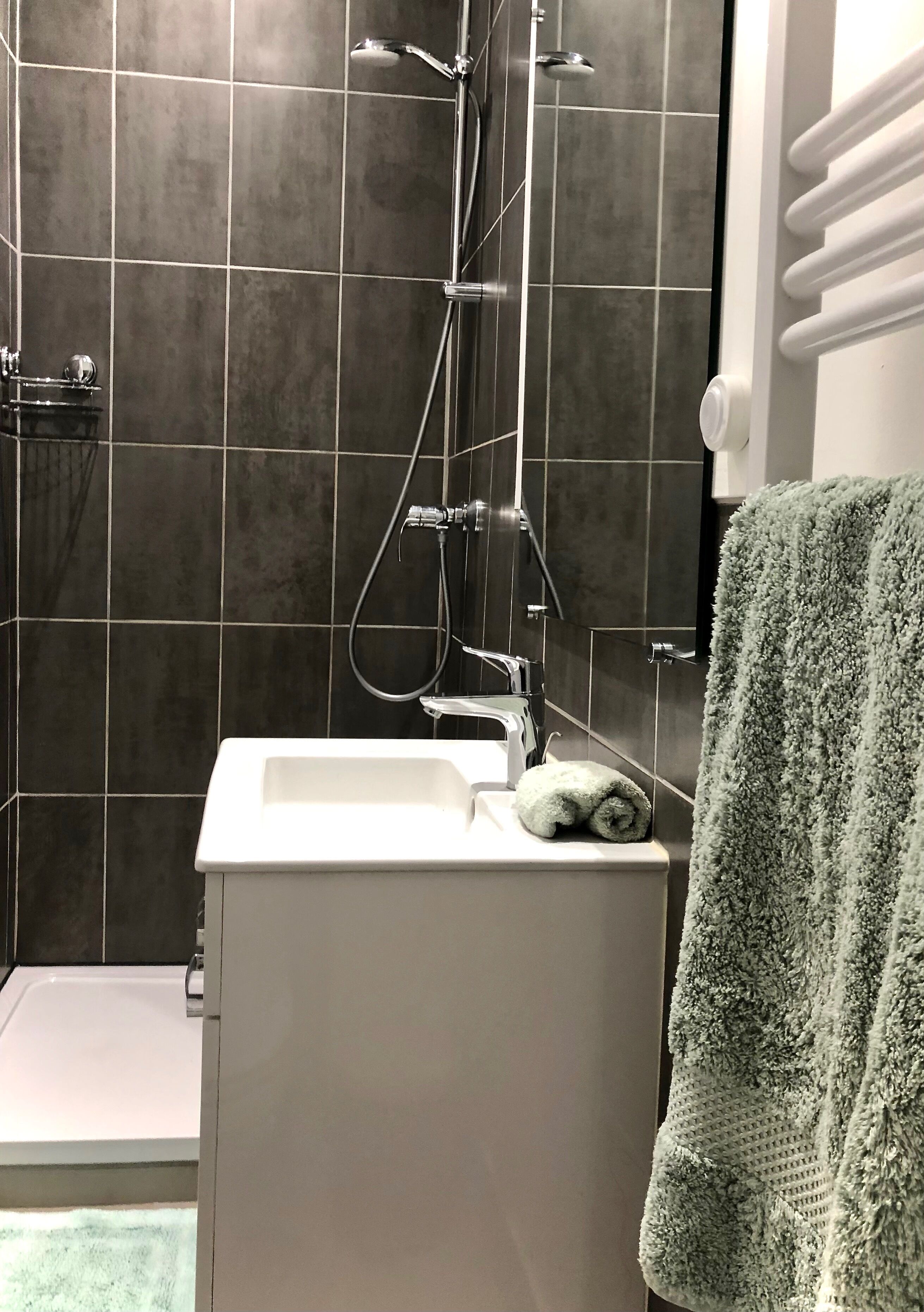A bathroom with a shower, a sink, and a towel rack.