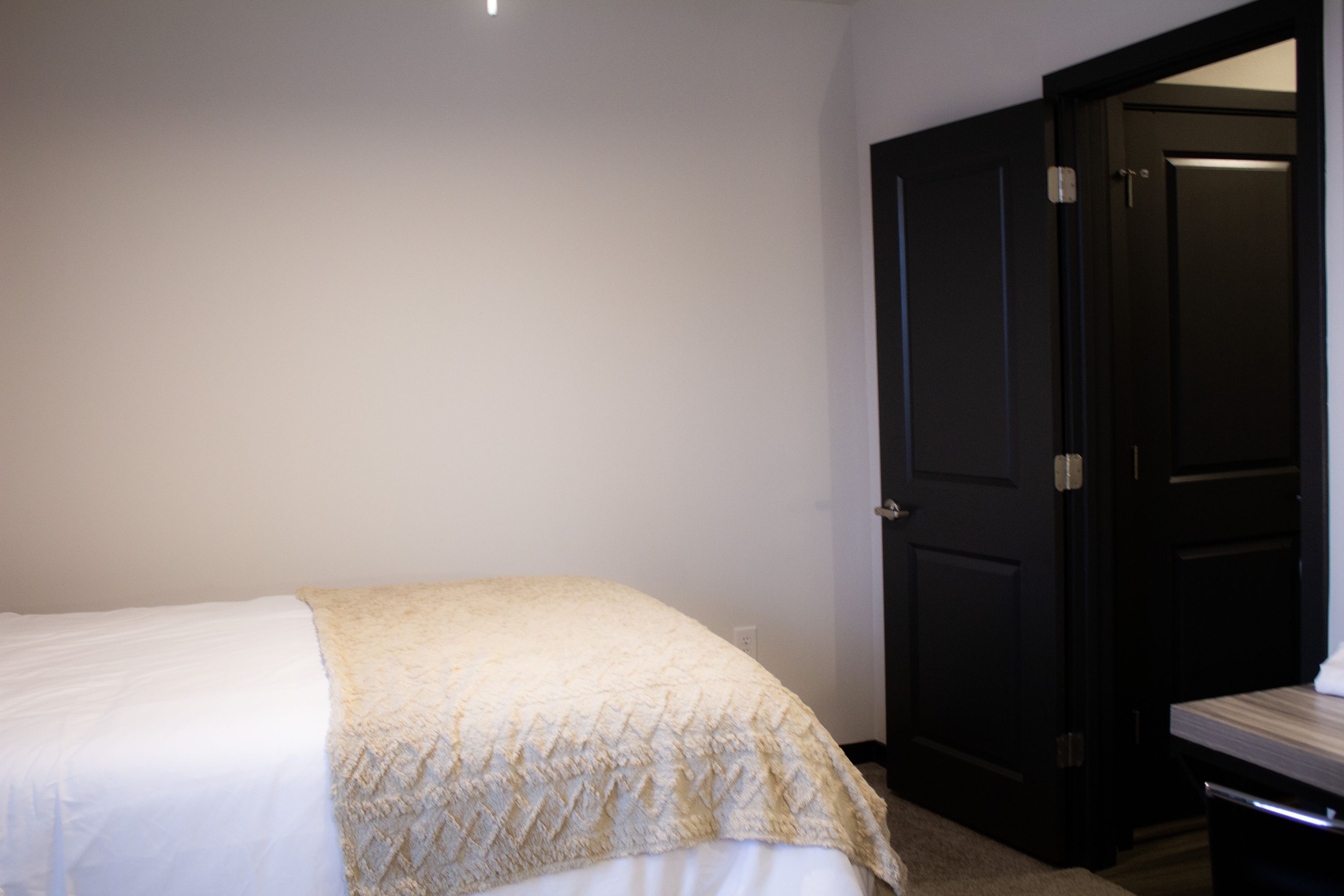 A bedroom with a bed, a dark door, and a small table.