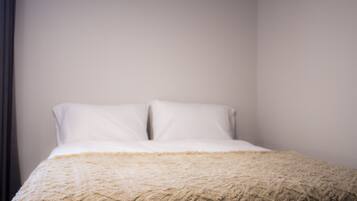 Una cama con una manta texturizada y dos almohadas en una habitación con paredes lisas.