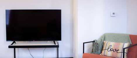 A modern living room with a flat-screen TV on a stand, a red sofa with a 'love' pillow, and a small black basket on the floor.