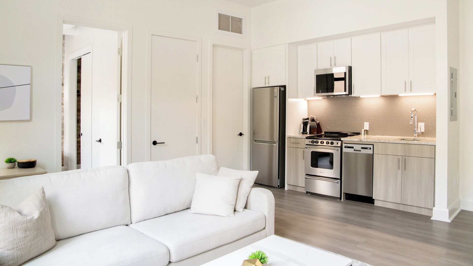A modern kitchen with stainless steel appliances, a white countertop, and a wooden floor.