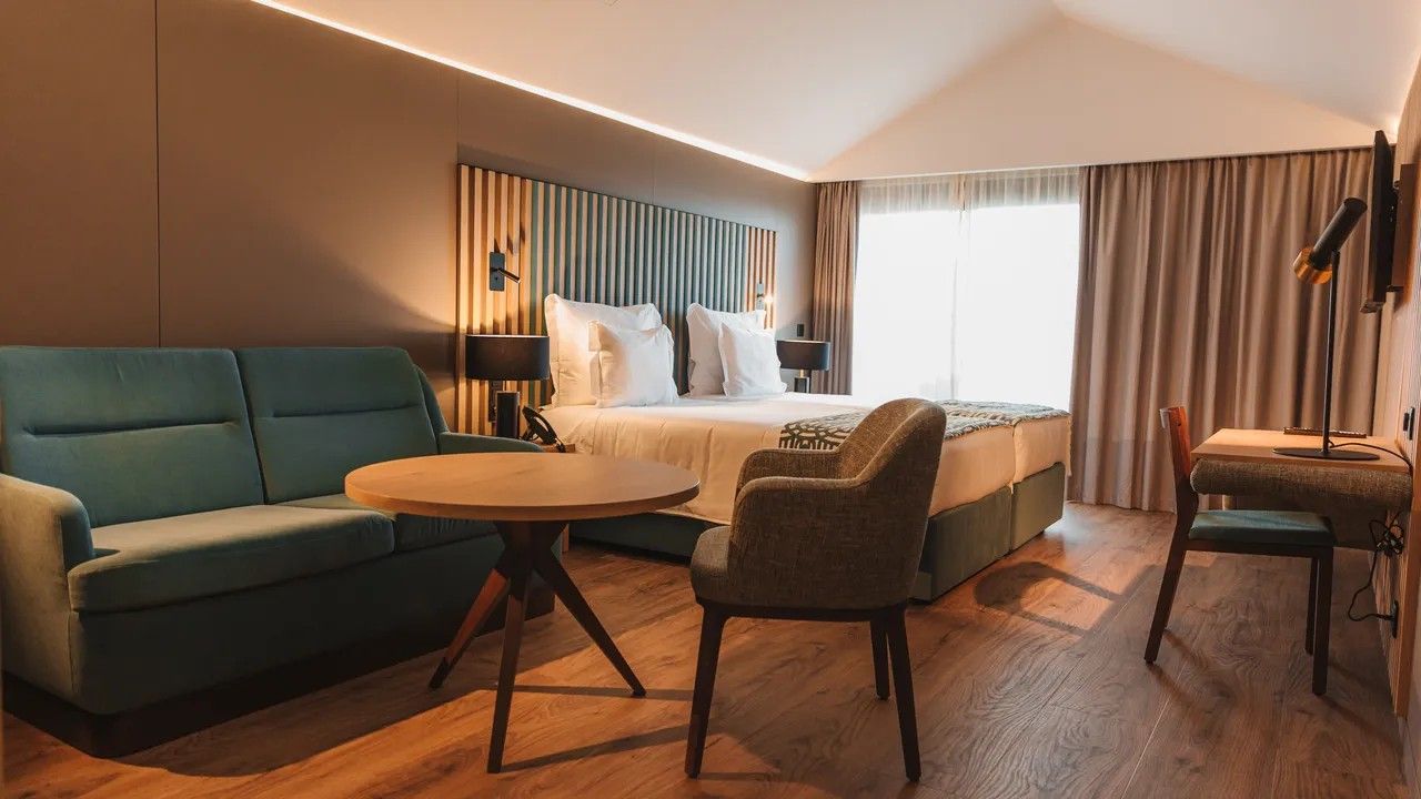 A modern hotel room with a bed, two sofas, a round table, and a chair.