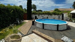 A swimming pool with a stone deck, surrounded by a garden and a tall tree. - Villa Nyvioni, Proche de la mer Avec Piscine et SPA (Agde)