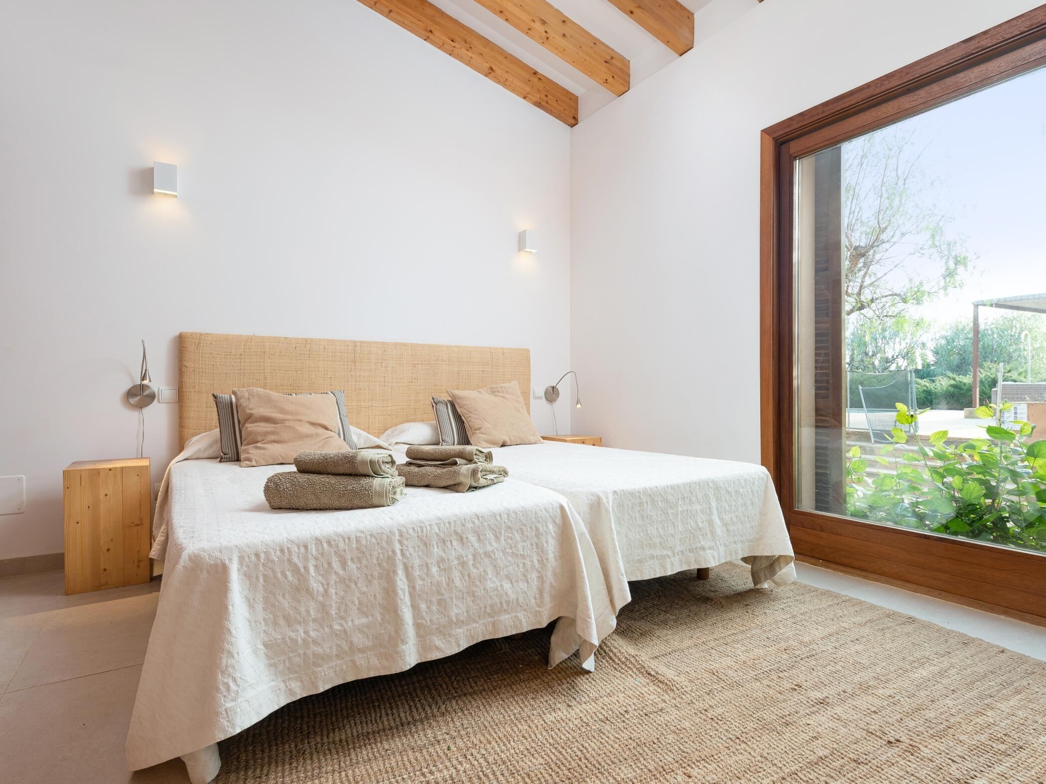 Ein Schlafzimmer mit einem großen Bett, zwei Nachttischen, einem Holz-Kopfteil und Blick auf Grün hinter einem großen Fenster.