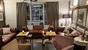 Una sala de estar acogedora con un sofá de cuero, sillones estampados y una mesa de centro de madera. Un ventanal con cortinas ofrece vistas a la calle.