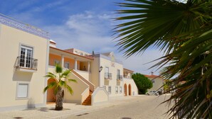 A street with buildings, a palm tree, and a car. - Red House (Amoreira-Óbidos)