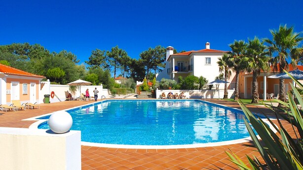 A swimming pool surrounded by palm trees and a white building with a red roof. - Red House (Amoreira-Óbidos)