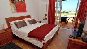 A bedroom with a bed, a nightstand, a TV, and a view of the outdoors. - Red House (Amoreira-Óbidos)