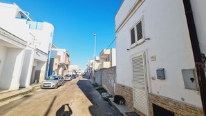 A narrow street lined with white buildings, some with balconies and shutters, and a few parked cars. - Ambra House (Porto Cesareo)