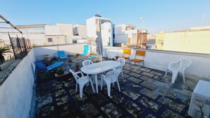 A rooftop terrace with a white table and chairs, potted plants, and a view of surrounding buildings. - Ambra House (Porto Cesareo)
