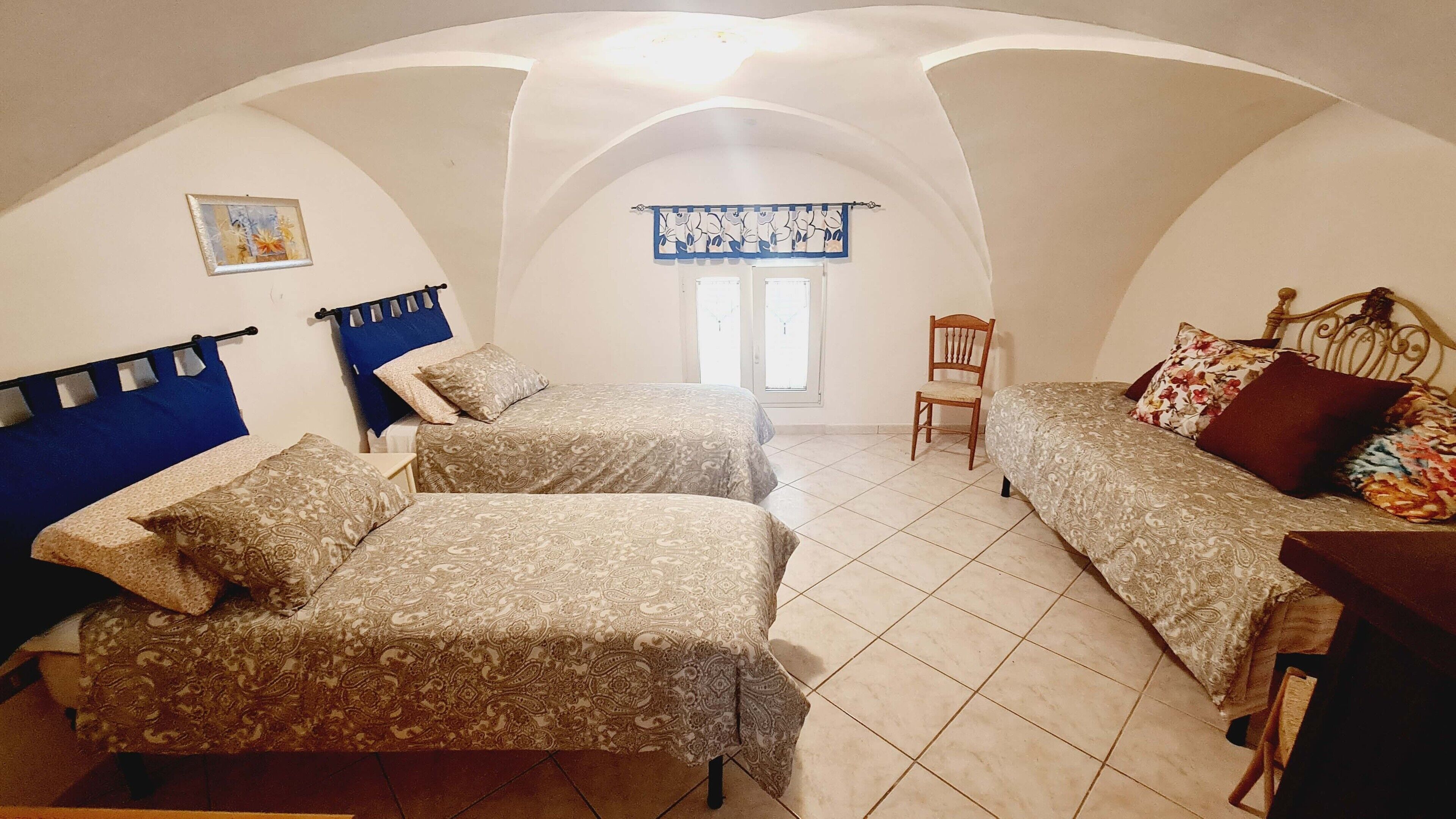A bedroom with two beds, a chair, and a window with curtains.