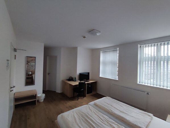 A bedroom with a bed, a desk, a chair, a radiator, and a window with blinds.