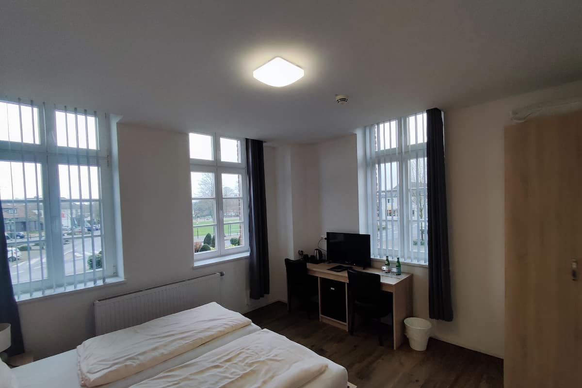 Une chambre d’hôtel avec deux lits, un bureau avec un ordinateur et de grandes fenêtres.