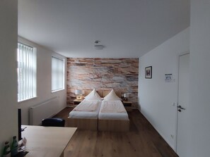 Une chambre avec un mur en pierre, un lit, des lampes de chevet, un radiateur et une porte.