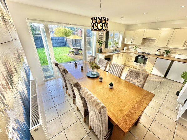 A modern kitchen with a large dining table, white cabinets, and a view of the backyard.