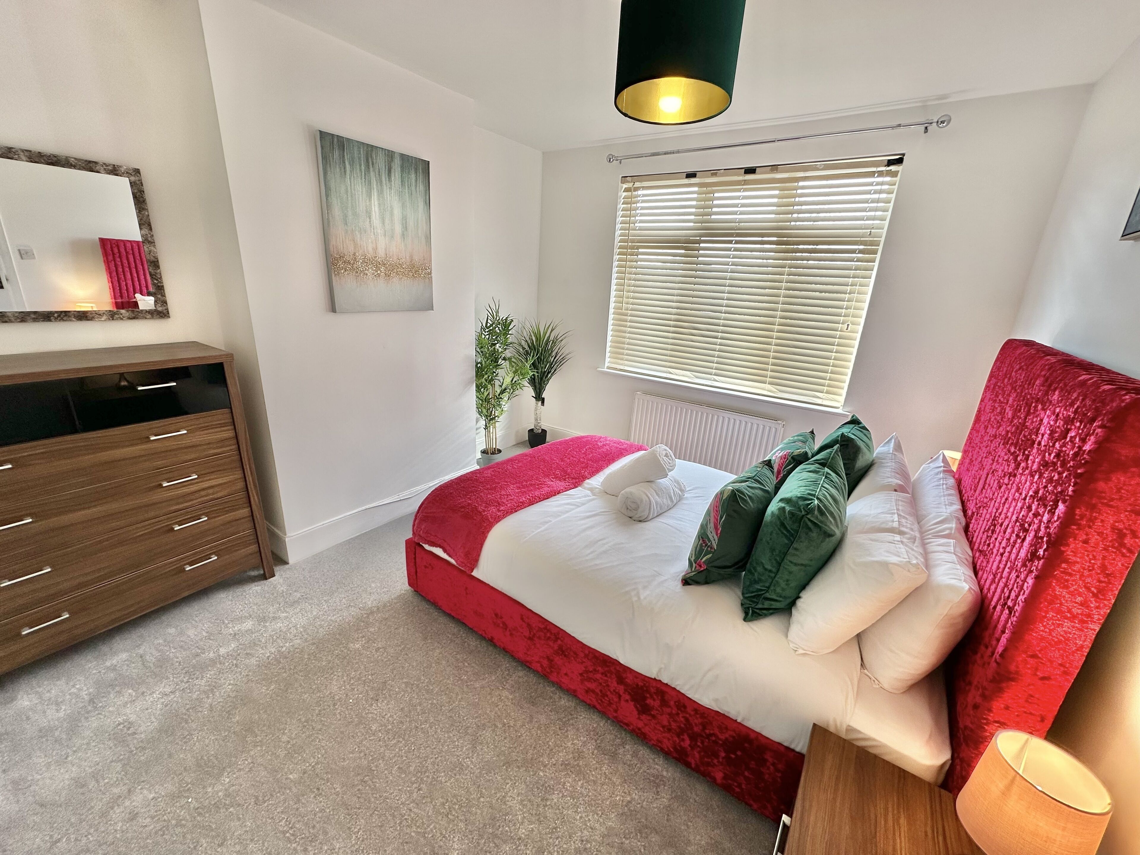Un dormitorio con cama, cómoda, espejo, ventana con persianas y un cuadro en la pared.