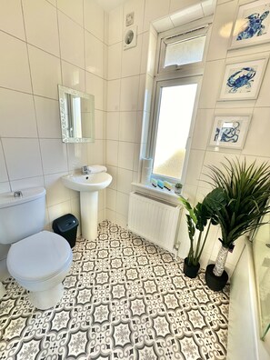 A bathroom with a toilet, sink, and radiator. There are decorative tiles on the floor and a window with a view.