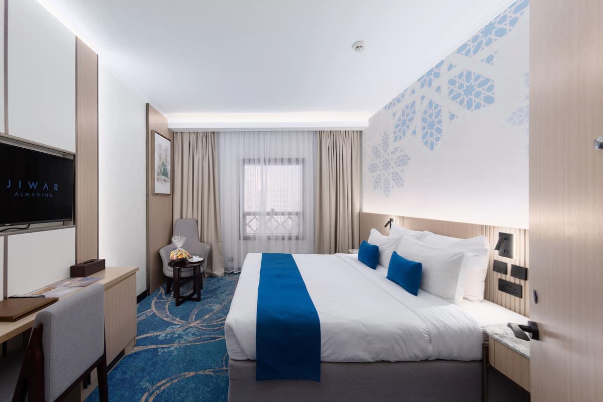 Een hotelkamer met een bed, een bureau, een stoel, een televisie en een raam met gordijnen.