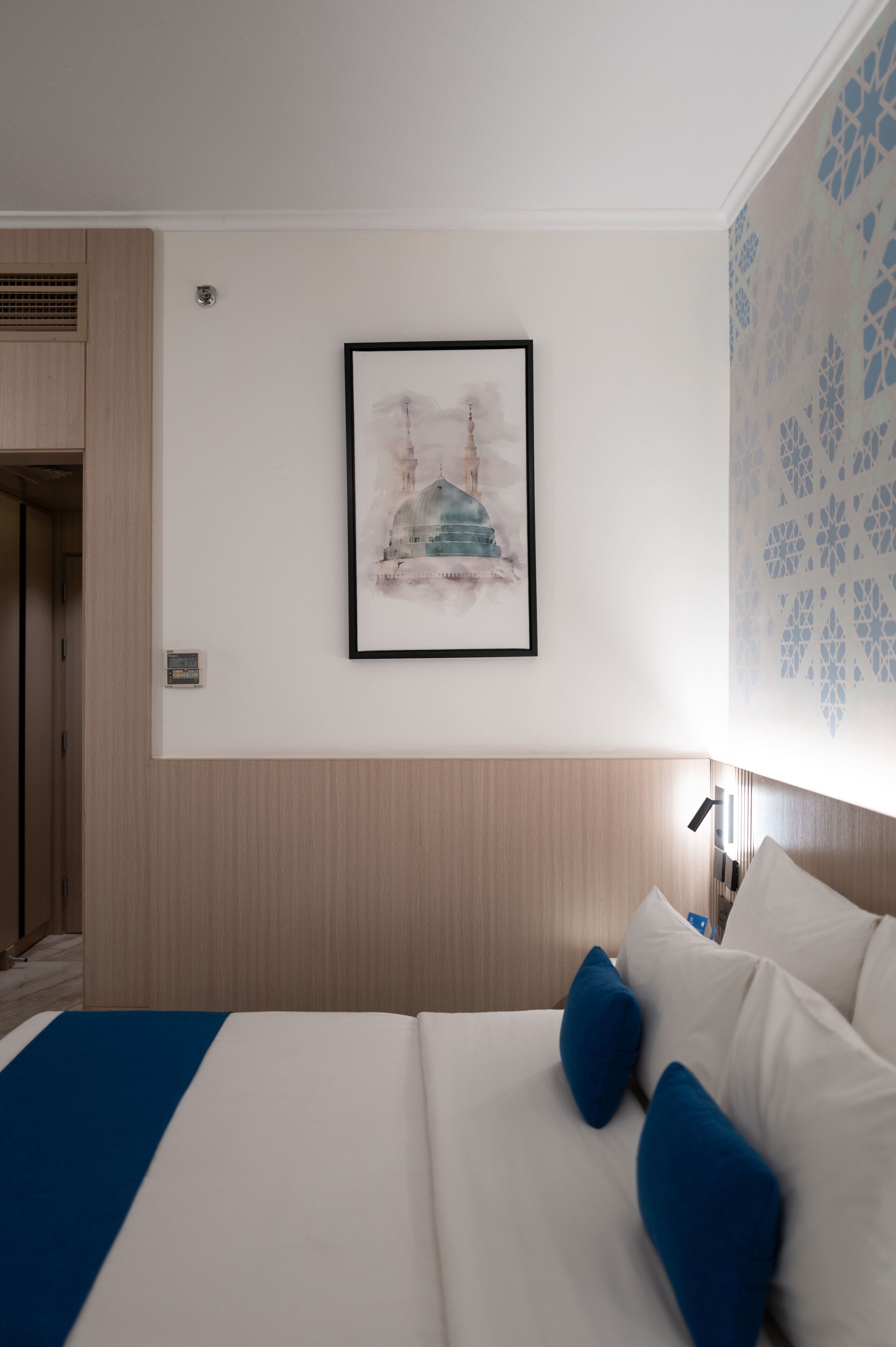 A hotel room with a bed, a framed picture on the wall, a nightstand, and a patterned wall.