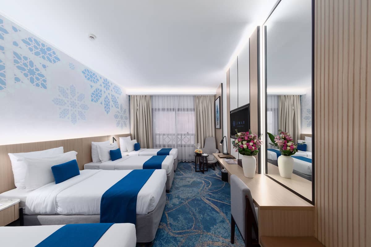 Een hotelkamer met twee bedden, een bureau, een stoel, een tafeltje, een spiegel en een raam met gordijnen.