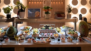 Een buffet met diverse gerechten en dranken, potplanten en een ingelijst menu.