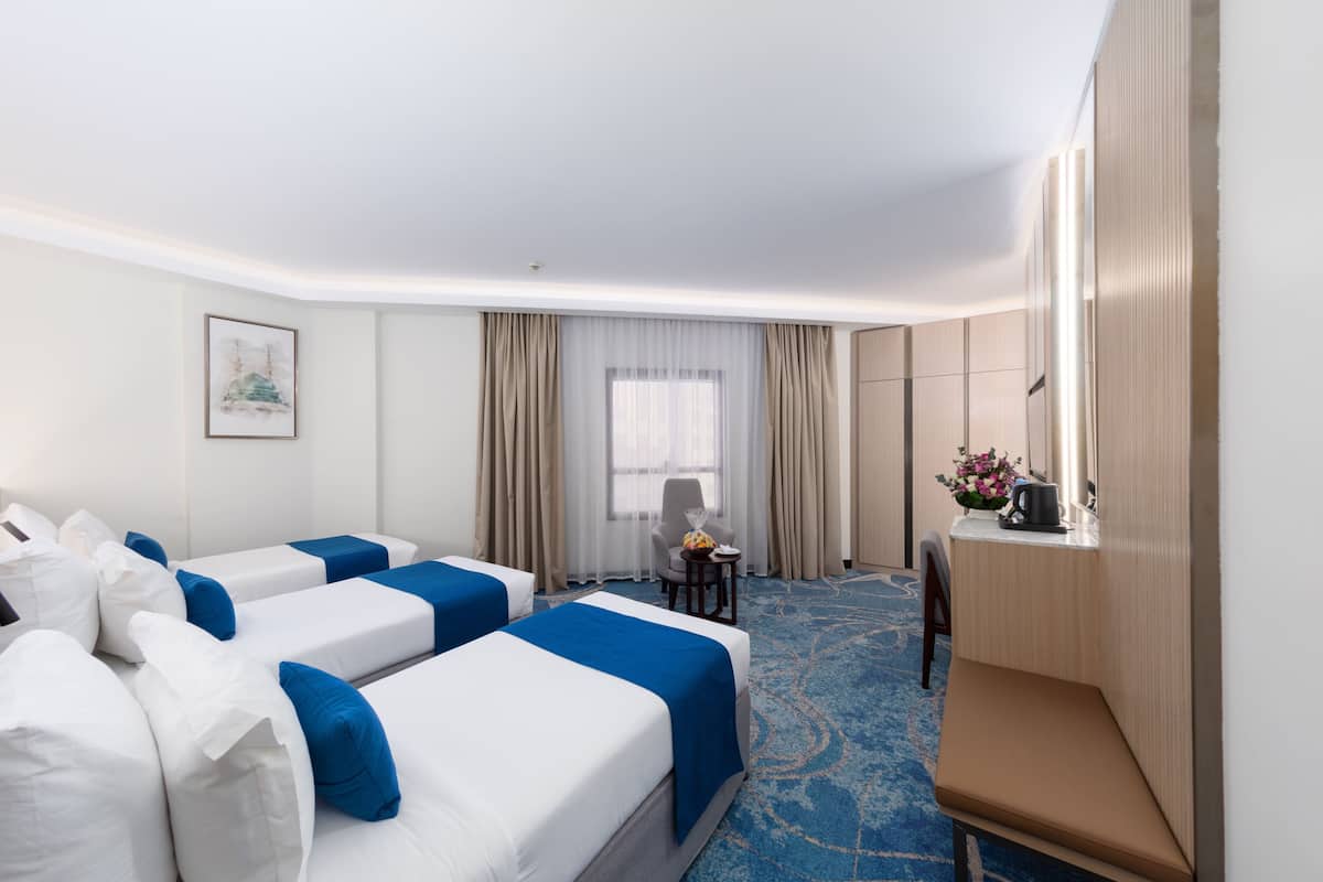 Hotelkamer met twee bedden, een bureau, een stoel, een tafeltje en een raam met gordijnen.