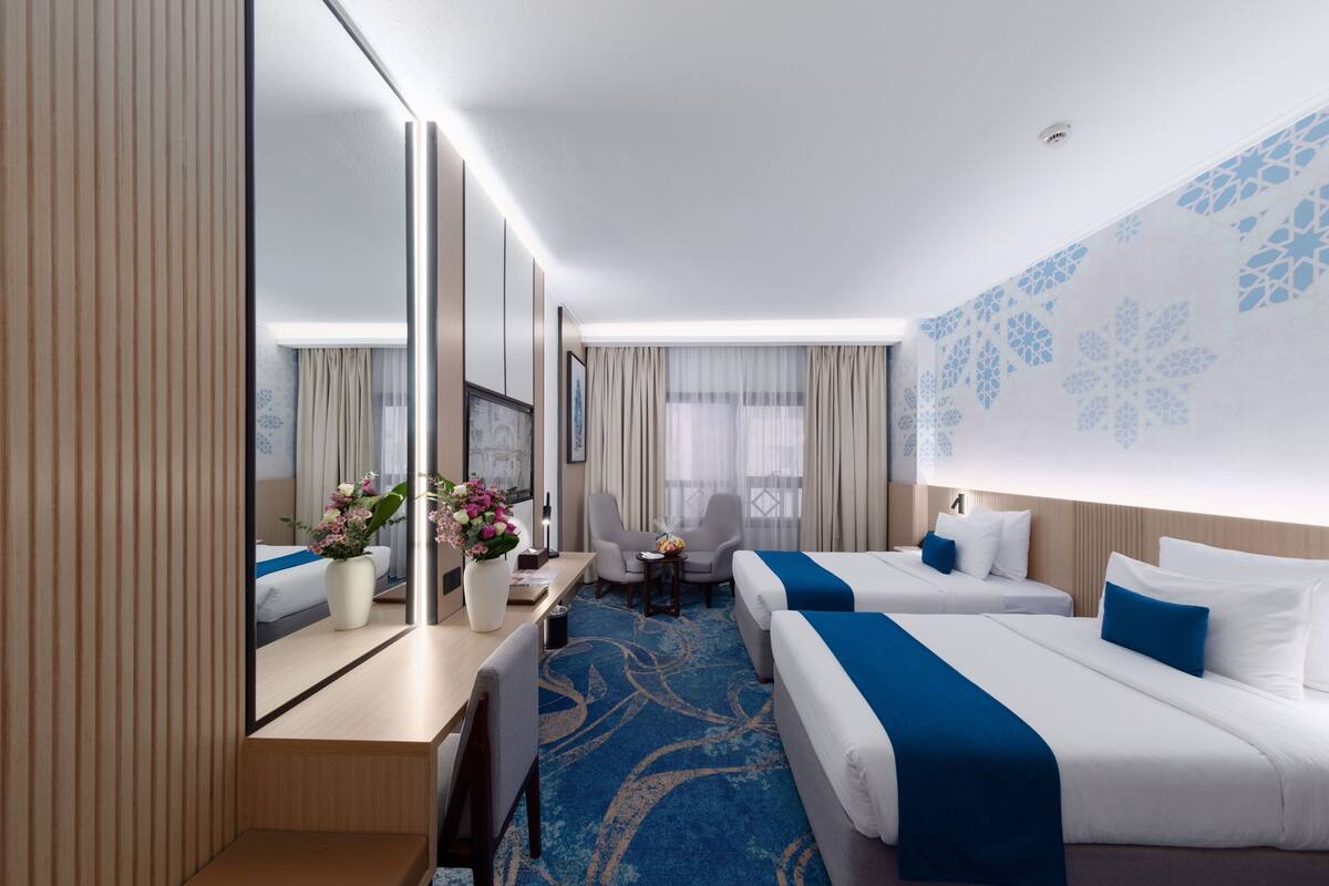 Een hotelkamer met twee bedden, een bureau, een stoel, een kleine tafel en een grote spiegel.