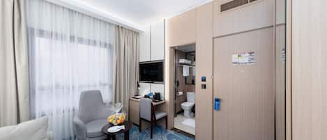 Habitación de hotel con cama, escritorio con computadora, televisor, ducha y armario.