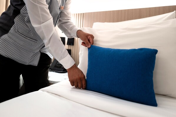 A person adjusting a blue pillow on a bed with white linens. - Jiwar Al Madina Hotel (Madinah)