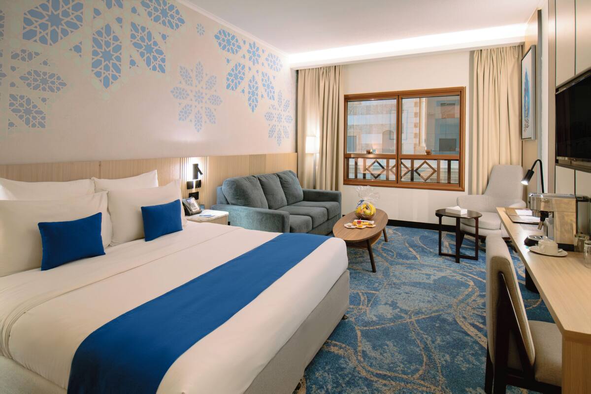 Een hotelkamer met een groot bed, een bank, een bureau, een televisie en een raam met uitzicht.