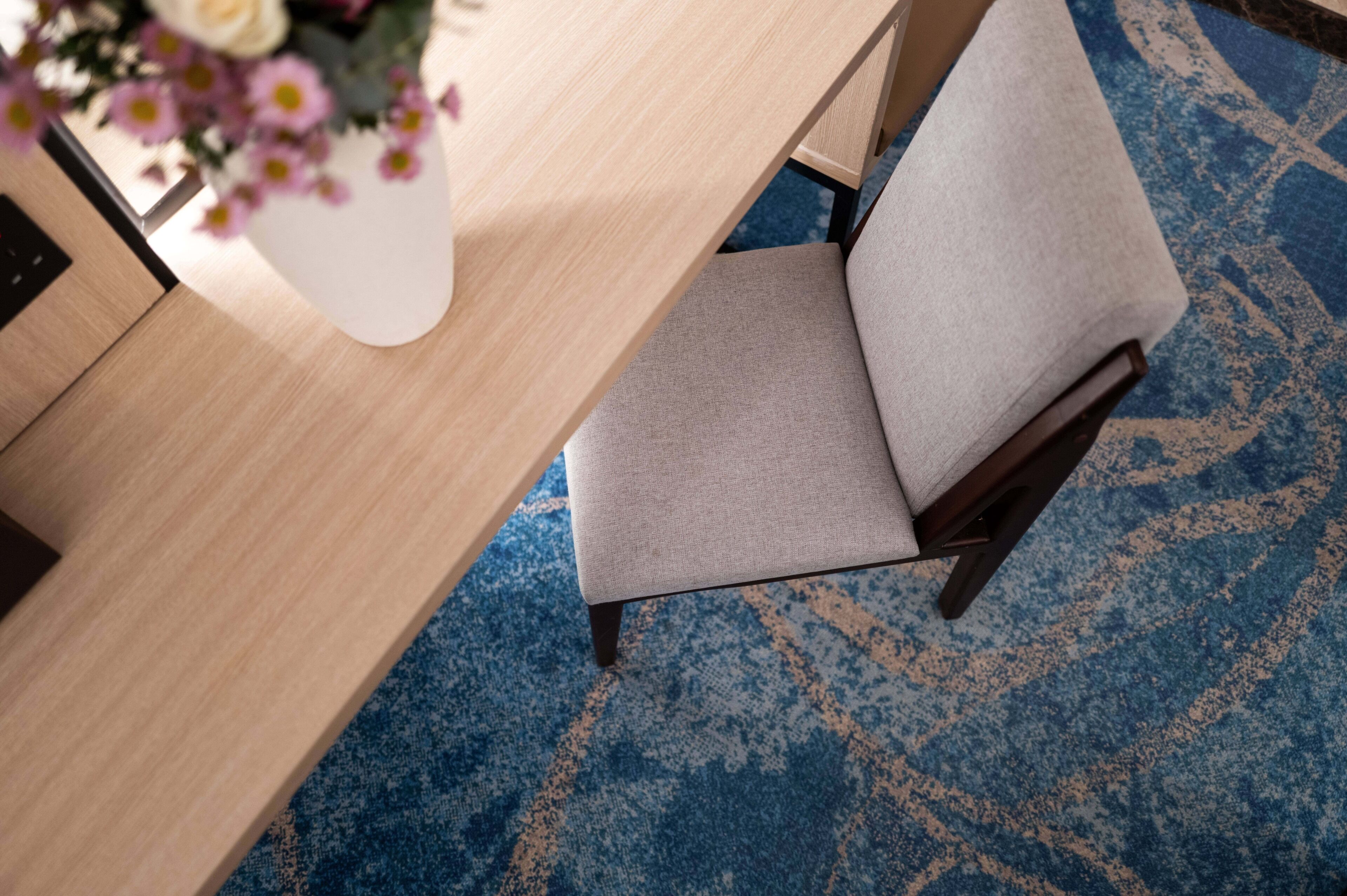 Una habitación con una mesa de madera, una silla tapizada de gris y una alfombra estampada.