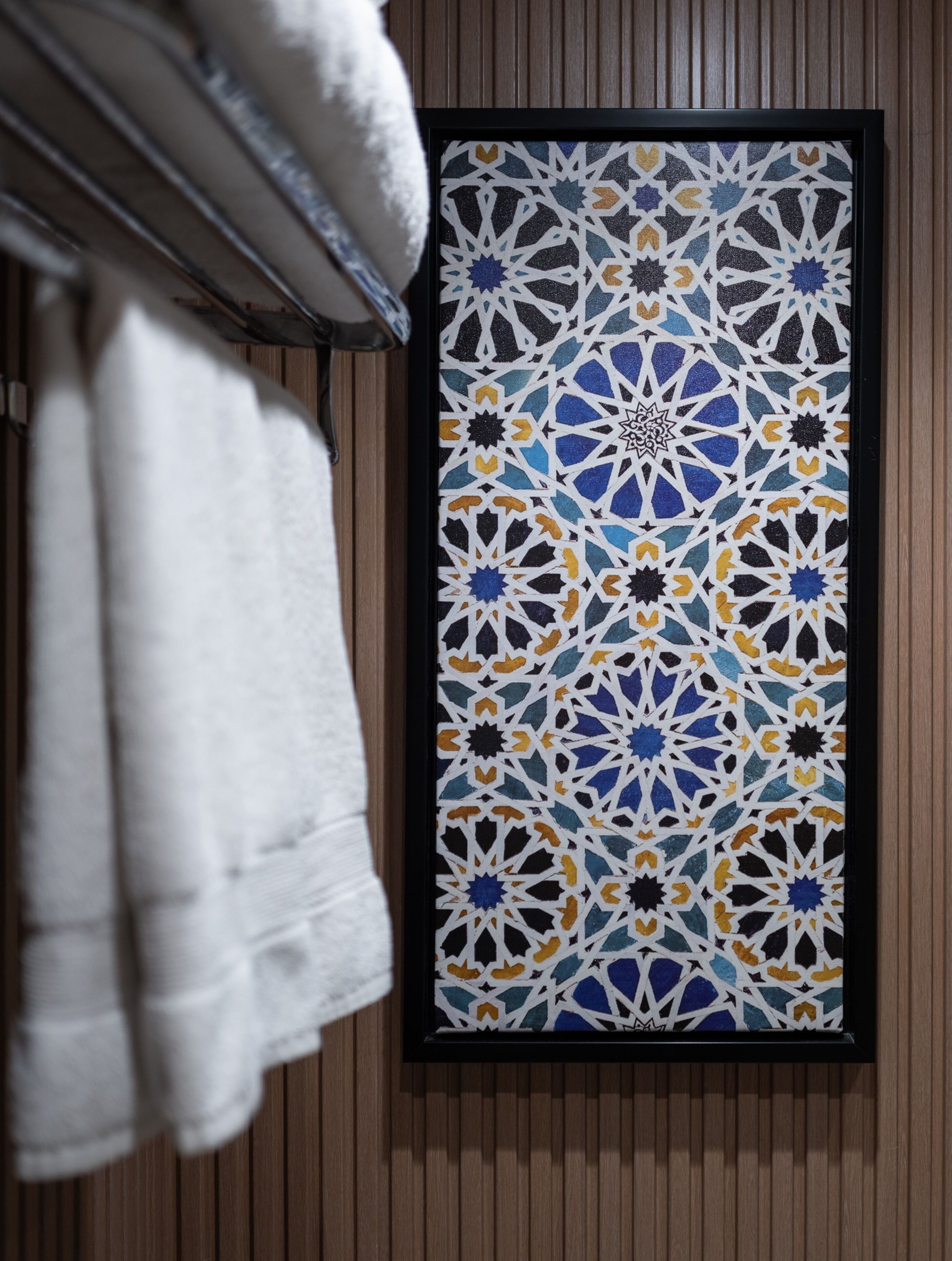 A framed geometric pattern on a wall, a towel rack with a white towel, and wooden paneling.