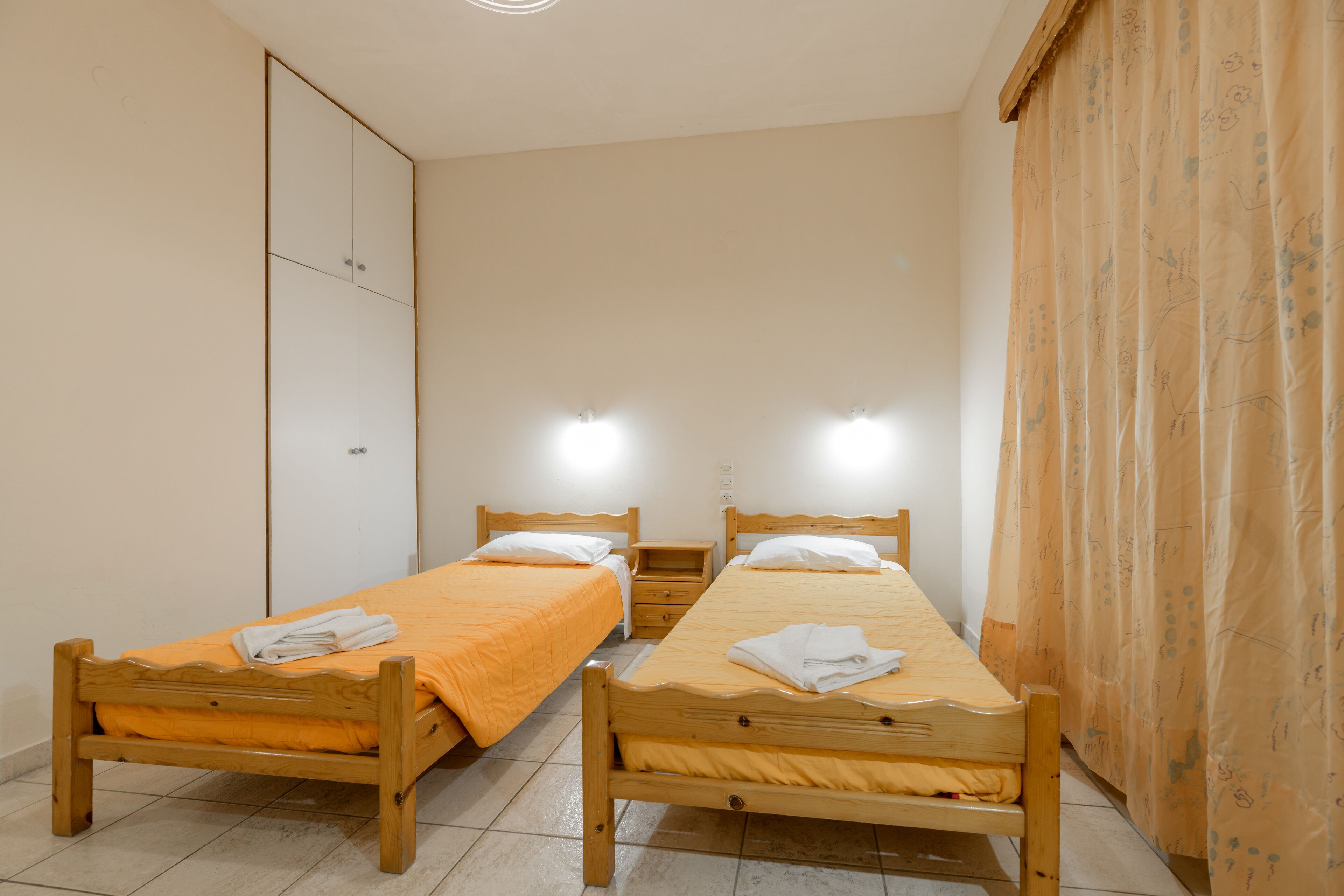 Une chambre à coucher avec deux lits en bois, une armoire et un rideau.