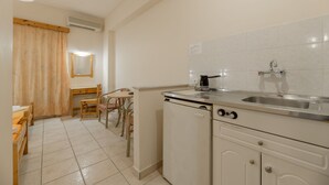 A compact kitchen with a sink, a coffee maker, and a small refrigerator. There is a dining area with a table and chairs. - Pink Panther Studios & Apartments (Zakynthos)
