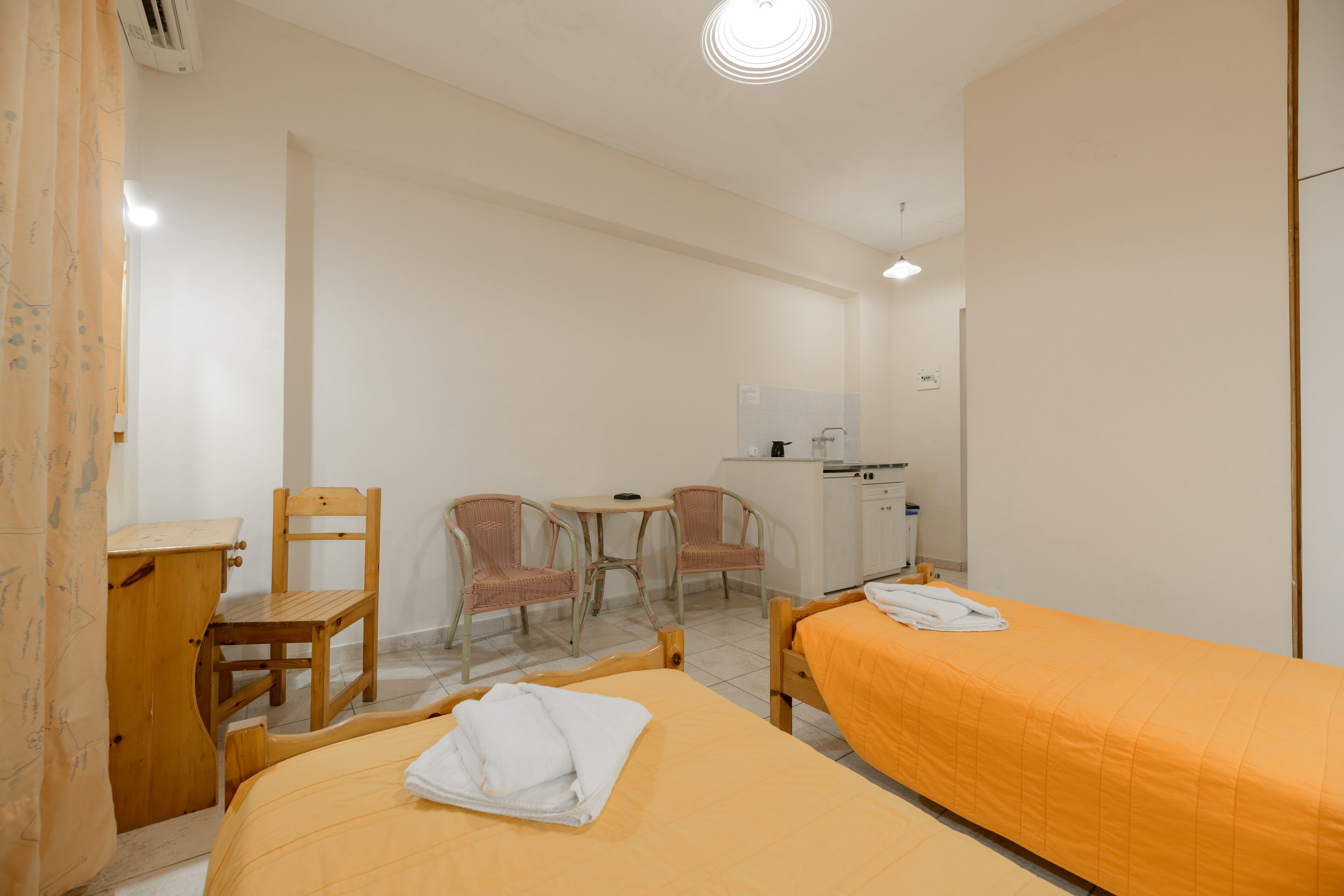 A hotel room with two beds, a desk, a chair, a small table, and a washing machine.