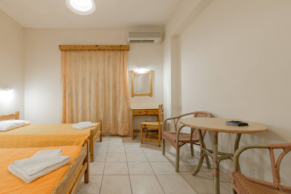 A hotel room with two beds, a desk, a chair, a small table, and a mirror.