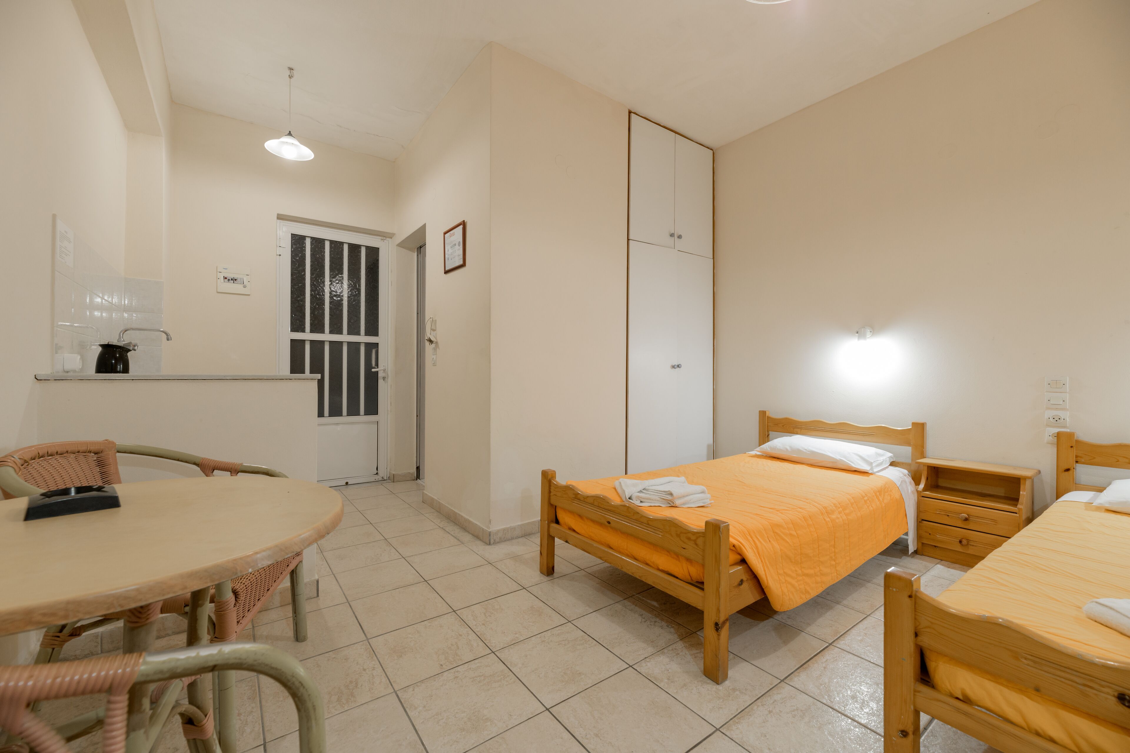 Een slaapkamer met twee enkele bedden, een houten tafel, een stoel, een kledingkast en een klein bureau met een lamp.