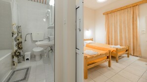 A bathroom with a shower, toilet, sink, and a small trash bin. - Pink Panther Studios & Apartments (Zakynthos)
